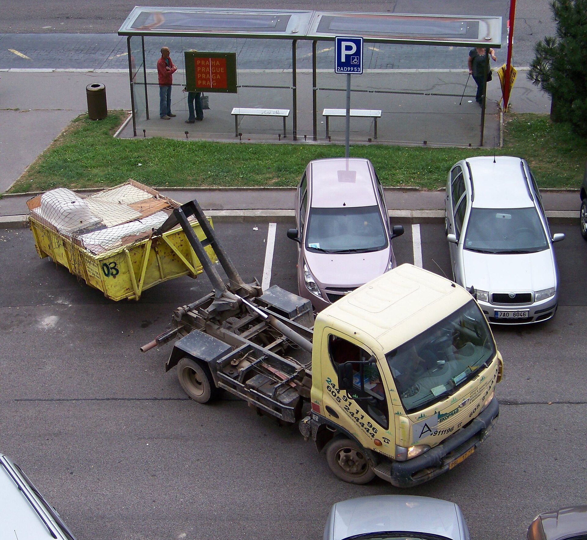 Hooklift truck loading a yellow construction waste dumpster container